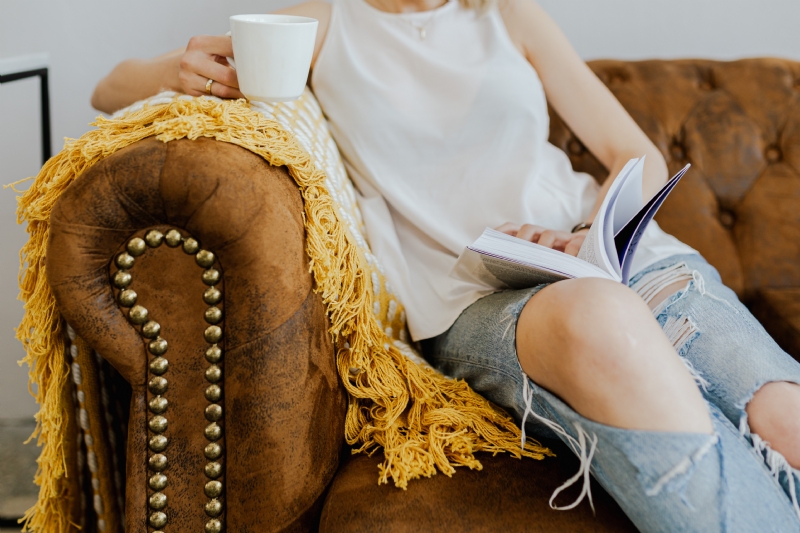 kaboompics_Woman with a cup of coffee & book, yellow blanket, blue jeans pants, brown couch.jpg 方案配图,客户爱好,阅读,